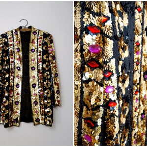 May include: A black sequined jacket with gold and pink accents. The jacket has a long, open front and is decorated with colorful beads and sequins.