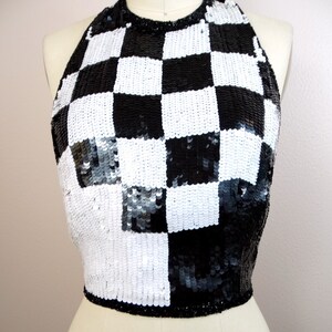 May include: A black and white checkered halter top made of sequins. The top is cropped and has a halter neckline.