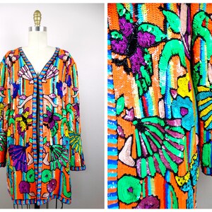 May include: A vibrant, sequined jacket in a longline style, featuring a V-neck and a black zipper. The jacket showcases a colorful design with orange, green, purple, and blue hues, adorned with floral and butterfly motifs.