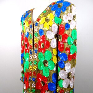 以下が含まれることがあります： カラフルな花柄のゴールドのラメジャケット。花は赤、青、緑、黄、ピンクのラメでできています。