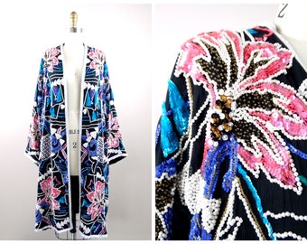 May include: A long black sequined jacket with a floral design. The jacket is decorated with pink, blue and white sequins and beads. The jacket has a white trim around the edges.