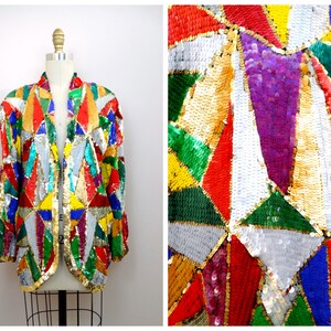 Pode incluir: Uma jaqueta colorida de lantejoulas com um padrão geométrico em tons de vermelho, verde, azul, amarelo, dourado e prata. A jaqueta tem uma frente longa e aberta e um caimento solto.