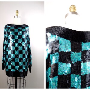 Puede incluir: Un su&eacute;ter de lentejuelas a cuadros de color azul verdoso y negro con mangas largas y cuello de barco.