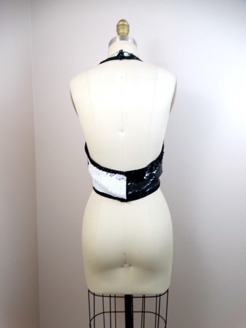 May include: A black and white halter top with sequins. The top is on a white dress form.