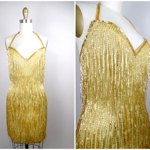 May include: A gold halter dress with a fringe design. The dress is made of sequins and beads.