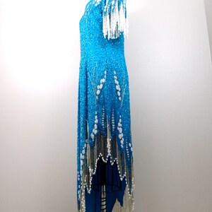 May include: A turquoise sequined dress with white beaded fringe. The dress has a scoop neck and short sleeves. The fringe is on the sleeves, hem, and neckline.