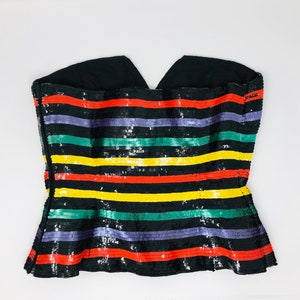 May include: A black strapless top with a multi-coloured striped pattern. The stripes are red, yellow, green, and purple. The top is made of sequins.