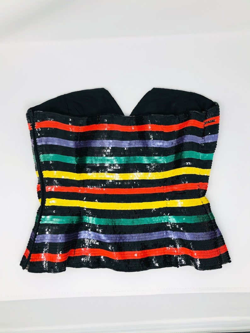 May include: A black strapless top with a multi-coloured striped pattern. The stripes are red, yellow, green, and purple. The top is made of sequins.