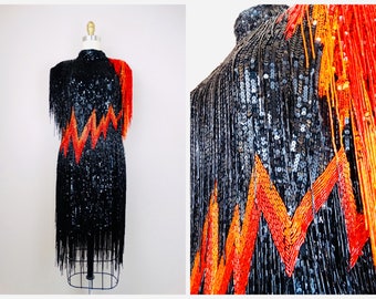 May include: A black sequined dress with orange and red fringe. The dress has a geometric pattern of zigzags.