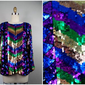 May include: A sequined jacket in a vibrant chevron pattern. The jacket features a spectrum of colors, including gold, green, purple, and blue. It has a round neckline and a zipper closure. The garment is displayed on a mannequin.