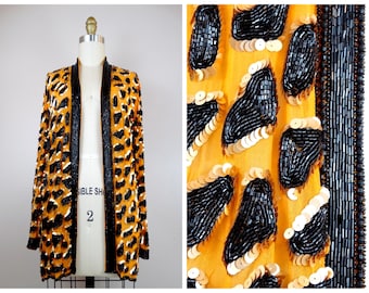 May include: A long-sleeved jacket with a leopard print pattern. The jacket is made of a sheer fabric and is embellished with black and gold sequins. The jacket has a black trim around the edges.