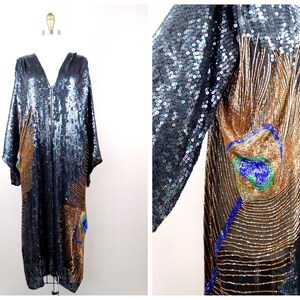 May include: A long, black sequined dress with a V-neck and long sleeves. The dress features a peacock feather design in gold, blue, and green sequins and beads. The dress is displayed on a mannequin.