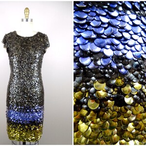 May include: A short, sleeveless dress made entirely of sequins. The sequins are arranged in a gradient pattern, starting with gold at the bottom, then black, and finally blue at the top.