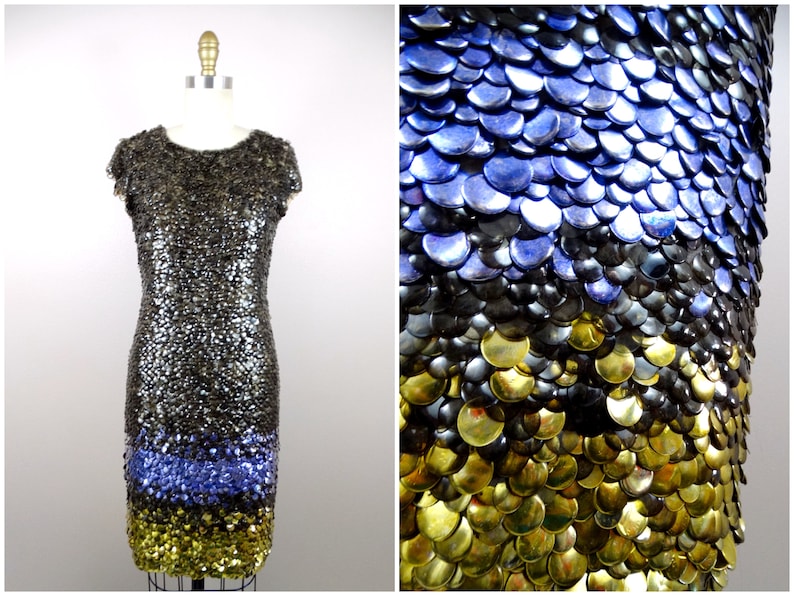 May include: A short, sleeveless dress made entirely of sequins. The sequins are arranged in a gradient pattern, starting with gold at the bottom, then black, and finally blue at the top.