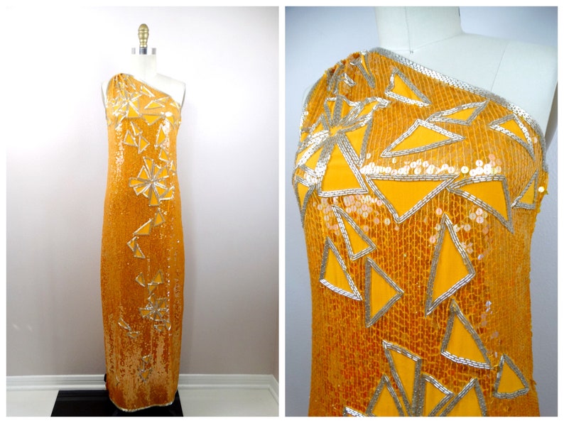 K&ouml;nnte beinhalten: Ein schulterfreies, bodenlanges Kleid mit einem geometrischen Muster aus goldenen Pailletten und silbernen Akzenten. Das Kleid ist aus einem gl&auml;nzenden Stoff gefertigt und hat eine figurbetonte Silhouette.