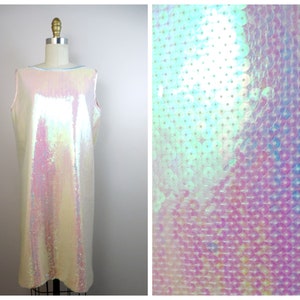 May include: A sleeveless iridescent white dress made of sequins. The dress has a scoop neck and a straight silhouette. The sequins are iridescent and reflect light in a variety of colors.
