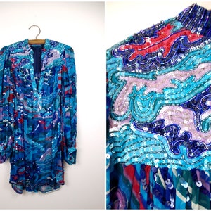 May include: A long-sleeved blue, purple, and red sequined blouse with a V-neckline. The sequins are arranged in a swirling pattern.