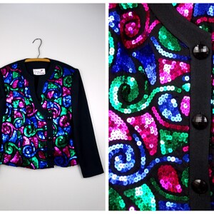 May include: Black jacket with long sleeves and a colorful sequined design on the front. The design features swirls of green, blue, and pink sequins. The jacket has black buttons and a black collar.