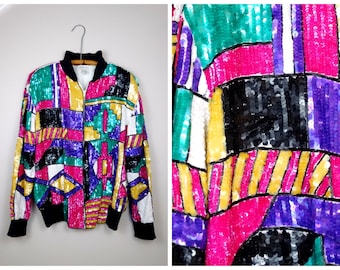 Puede incluir: Una chaqueta bomber de lentejuelas de colores con un patrón geométrico en tonos de rosa, morado, verde, amarillo, negro y blanco.
