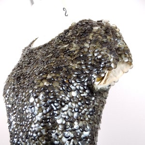 May include: A close-up of a silver and black dress with a unique design made of overlapping scales. The dress is on a white mannequin.