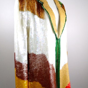 May include: A sequined jacket with a colorful geometric pattern in shades of white, brown, yellow, and red. The jacket has a green and gold trim and a V-neck.