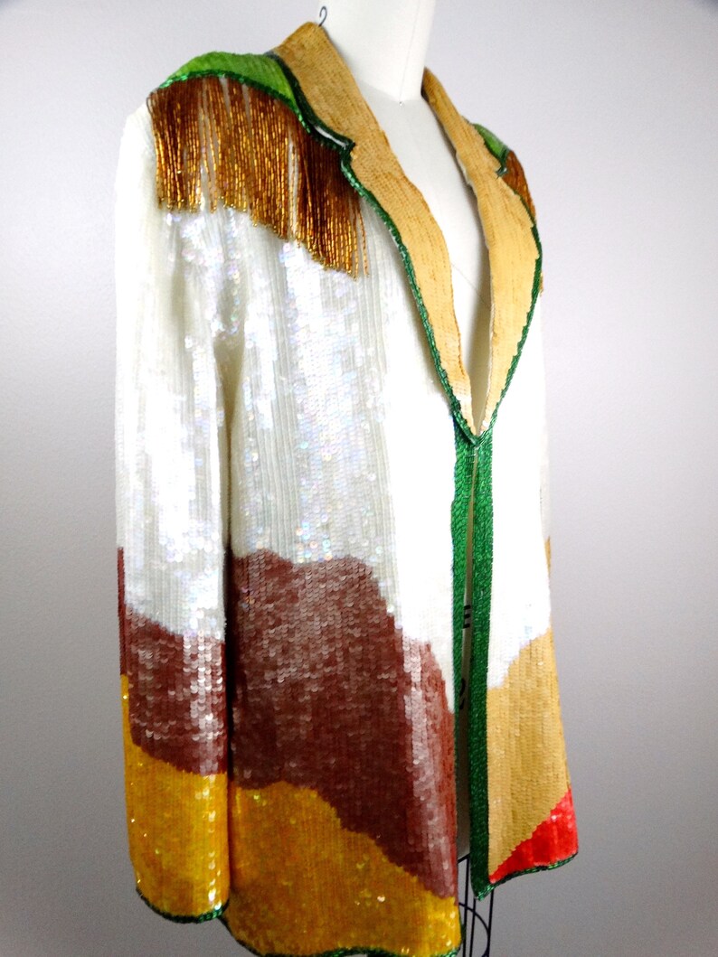 May include: A sequined jacket with a colorful geometric pattern in shades of white, brown, yellow, and red. The jacket has a green and gold trim and a V-neck.