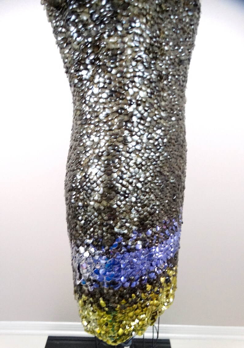 May include: A silver sequined dress with a blue and gold sequined trim. The dress is on a mannequin.