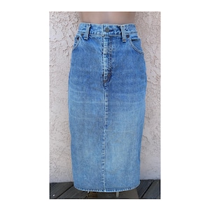 May include: A high-waisted midi-length denim skirt in a medium blue wash. The skirt features a classic five-pocket design, a metal button closure at the waistband, a zippered fly, and visible vertical seam detailing running down the front center.