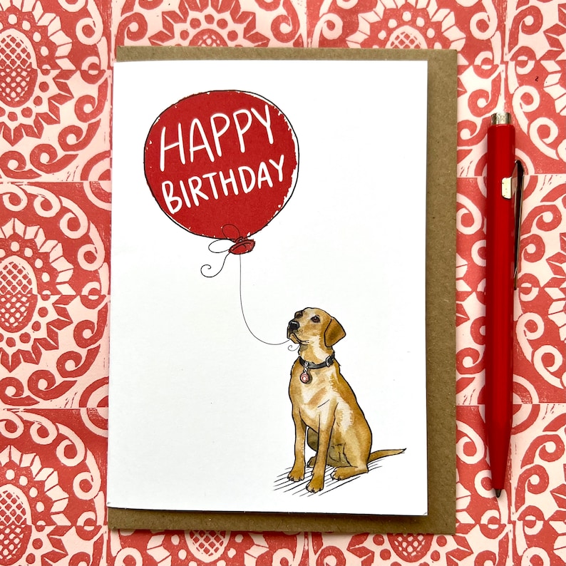 May include: A greeting card with a red balloon that says "Happy Birthday" and a yellow Labrador Retriever looking up at the balloon.