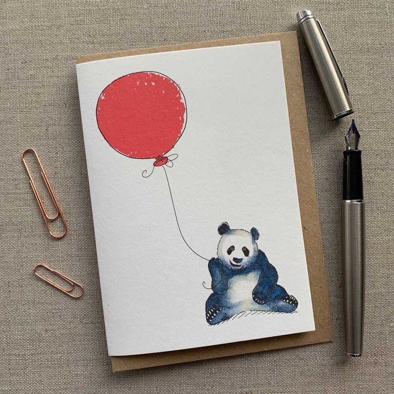 May include: A white card with a black and white illustration of a panda bear holding a red balloon. The panda is sitting on the ground and the balloon is floating in the air. The card is blank and ready for a message.