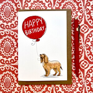 May include: A greeting card with a red balloon that says "Happy Birthday" and a brown and white dog looking up at the balloon.