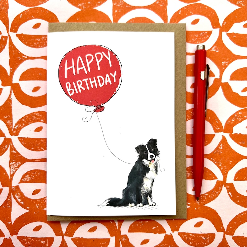 May include: A birthday card featuring a black and white border collie holding a red balloon that says "Happy Birthday".