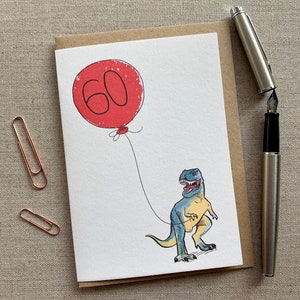 May include: A greeting card with a red balloon that says "60" and a blue and yellow dinosaur holding the string of the balloon.