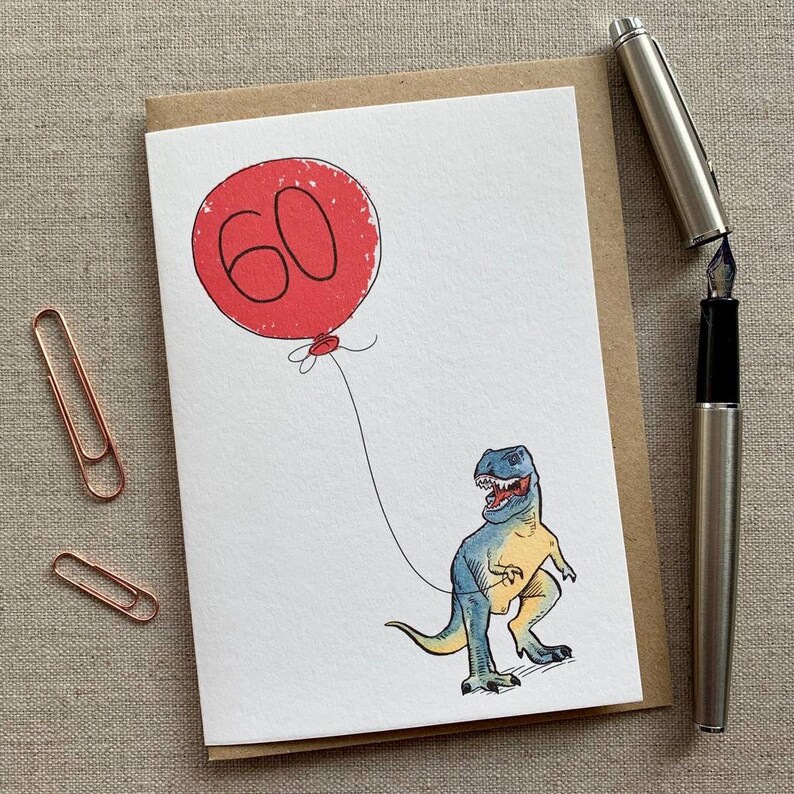 May include: A greeting card with a red balloon that says "60" and a blue and yellow dinosaur holding the string of the balloon.