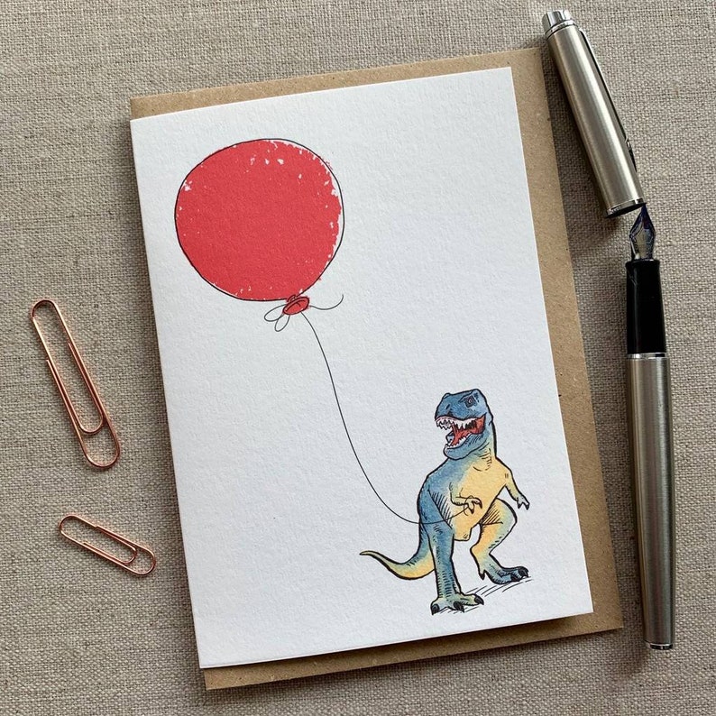 May include: A greeting card with a cartoon illustration of a blue and yellow dinosaur holding a red balloon.