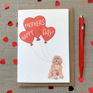 Puede incluir: Una tarjeta del Día de la Madre con un perro marrón sosteniendo tres globos rojos en forma de corazón. Los globos tienen las palabras "Happy Mother's Day". La tarjeta está en un sobre marrón con confeti de corazón rojo y un bolígrafo rojo.