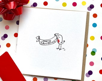 May include: A white square greeting card with a cartoon bird holding a banner that reads "merry christmas!". The card is on a white and brown surface, with a red bow and a red card in the background. The card is a festive holiday item.