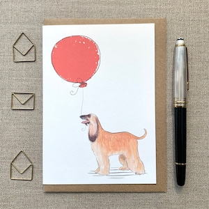 May include: A greeting card featuring a watercolour illustration of an Afghan Hound dog with a red balloon. The dog is looking up at the balloon, which is tied to its mouth.