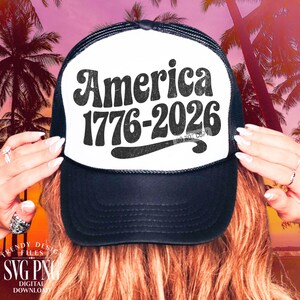 May include: Black and white trucker hat with the text "America 1776-2026" in a retro font. The hat has a white front panel and a black mesh back. The image is set against a tropical sunset backdrop.