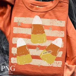 May include: An orange crewneck sweatshirt featuring a distressed graphic print of three candy corn pieces arranged over horizontal stripes and small stars. The design includes a white, orange, and yellow color palette with a weathered texture.
