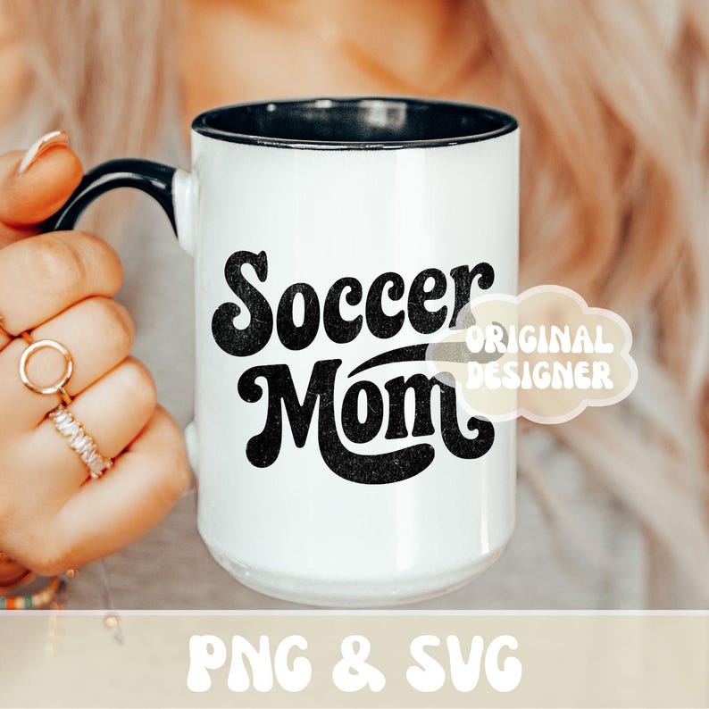 Op de afbeelding: Witte keramische mok met een zwarte binnenkant en handvat. De mok heeft de woorden "Soccer Mom" in een vet, zwart retro lettertype. Een kleine, lichtgekleurde wolk-vormige afbeelding met de woorden "ORIGINAL DESIGNER" staat rechts.
