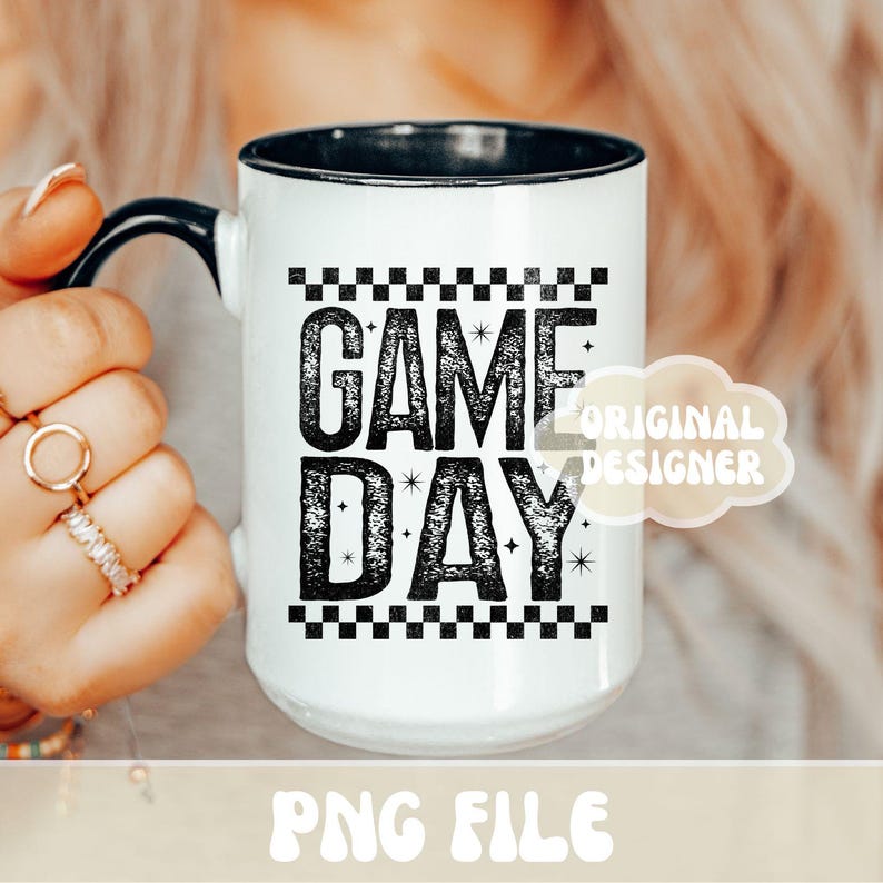 K&ouml;nnte beinhalten: Wei&szlig;er Keramikbecher mit schwarzem Innenraum und Henkel. Der Becher zeigt den Text "GAME DAY" in einer kr&auml;ftigen, verwitterten Schrift, mit einem Schachbrettmuster &uuml;ber und unter dem Text. Der Becher wird von einer Person gehalten.