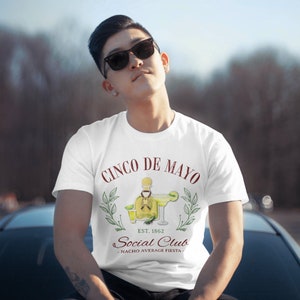 Puede incluir: Camiseta blanca con un dise&ntilde;o de Cinco de Mayo. El gr&aacute;fico incluye texto, una margarita y una botella de tequila. El texto dice "Cinco de Mayo Social Club - Nacho Average Fiesta".