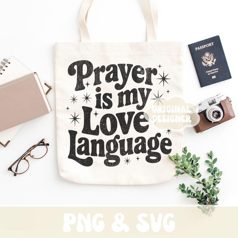 Op de afbeelding: Een cr&egrave;mekleurige draagtas met de zwarte tekst "Prayer is my Love Language". De afbeelding bevat een paspoort, een camera, een bril, een notitieboek en groen. Het ontwerp heeft ster-accenten rond de tekst.