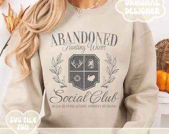 Op de afbeelding: Een beige sweatshirt met de tekst "ABANDONED Hunting Wives Social Club" en de tekst "HELLO HUNTING SEASON, GOODBYE HUSBAND."