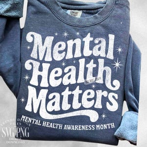 May include: A navy blue sweatshirt with the words "Mental Health Matters" in large, white, distressed lettering. The phrase "Mental Health Awareness Month" is printed below. The sweatshirt has a crew neck and long sleeves.