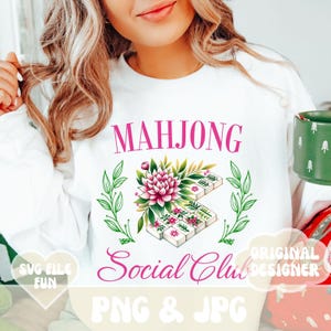 Puede incluir: Una sudadera blanca con un dise&ntilde;o floral rosa y el texto "Mahjong Social Club" en rosa. El dise&ntilde;o incluye una flor y fichas de mahjong. El texto "SVG File Fun" est&aacute; en un coraz&oacute;n rosa y el texto "Original Designer" est&aacute; en rosa.