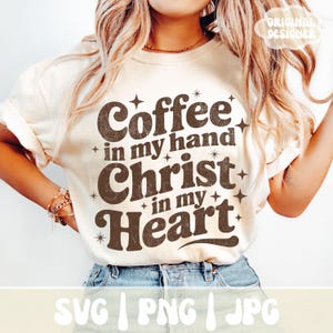 May include: Cream-colored t-shirt with the text "Coffee in my hand, Christ in my Heart" in brown, retro-style lettering. The design includes star accents. The bottom of the shirt shows the text "SVG | PNG | JPG".