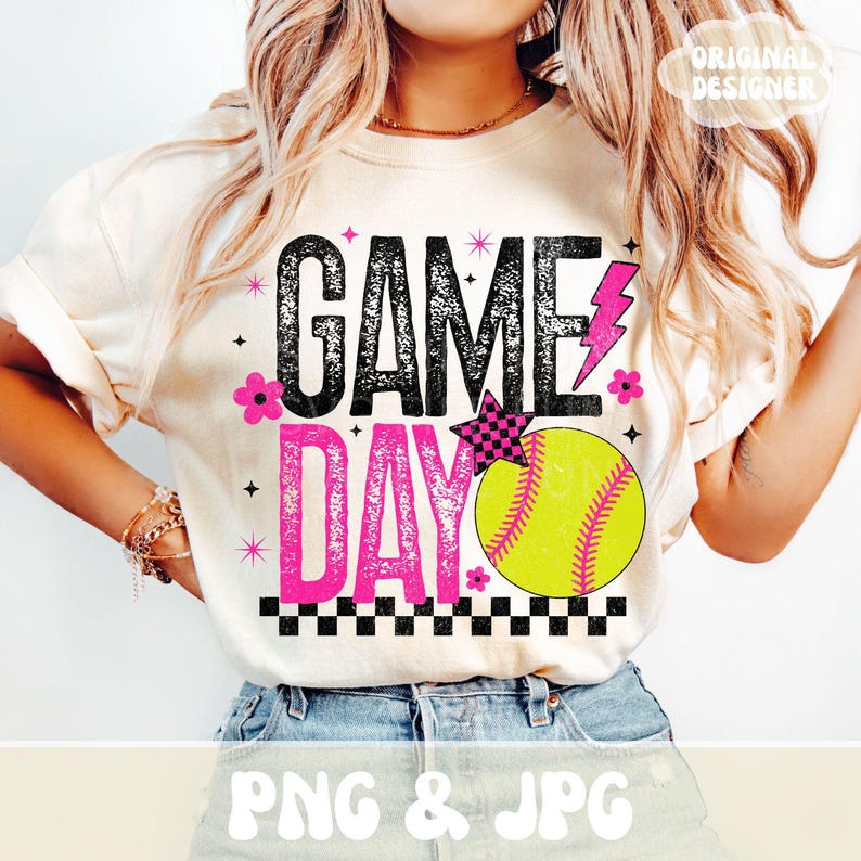 May include: Cream-colored t-shirt with the words "GAME DAY" in black and pink, featuring a softball graphic. The design includes a pink lightning bolt, a checkered star, and pink flowers. The words "PNG & JPG" are at the bottom.