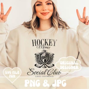May include: A beige sweatshirt with a black graphic design that says "Hockey Moms Social Club Loud and Proud". The graphic includes a hockey helmet, sticks, and a wine glass.